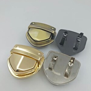 May include: Four metal clasps in different finishes: gold, brass, silver, and black. Each clasp has a shield shape with a hinged top.