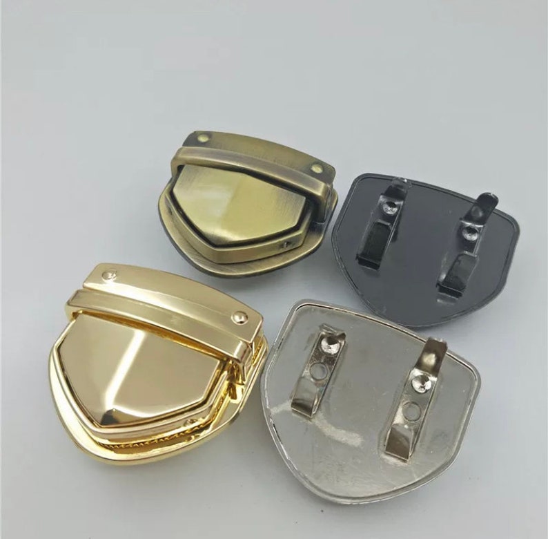 May include: Four metal clasps in different finishes: gold, brass, silver, and black. Each clasp has a shield shape with a hinged top.