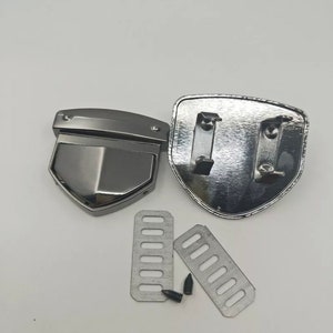 May include: A set of silver metal belt buckle hardware. The set includes two shield-shaped pieces, two rectangular pieces with holes, and a small silver screw.