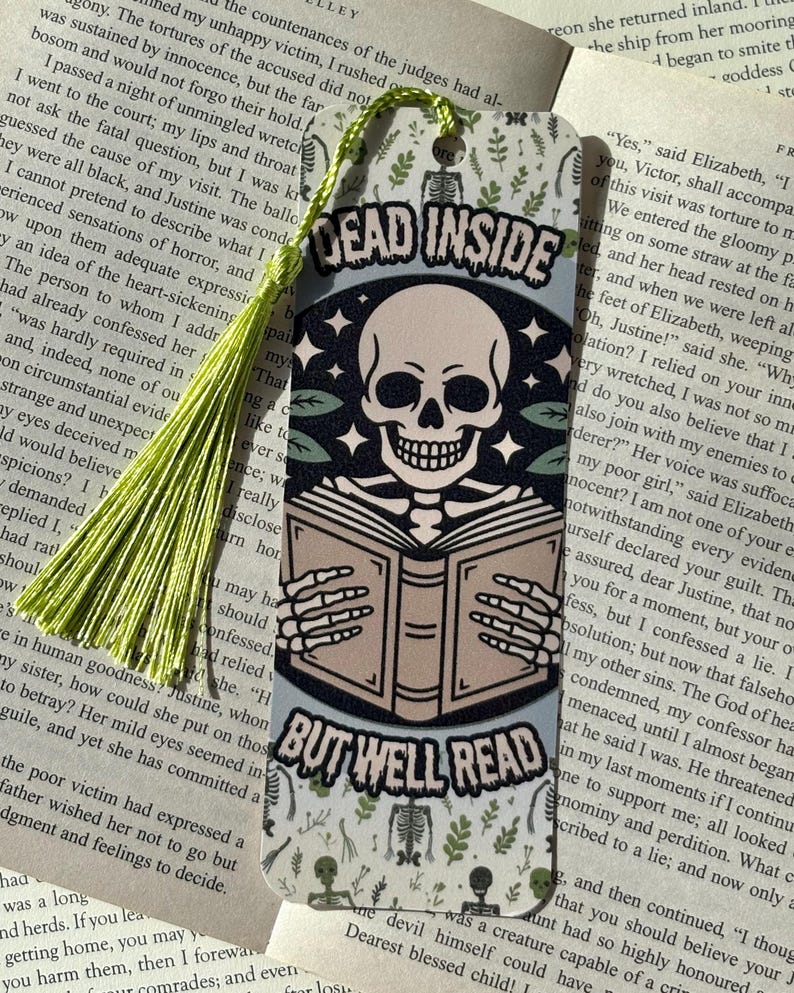 以下が含まれることがあります： 本を読む骸骨が描かれたブックマークで、「DEAD INSIDE BUT WELL READ」の文字が入っています。 ブックマークには緑色のタッセルと、骸骨と葉の装飾模様が付いています。