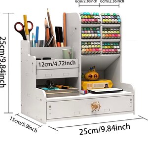 May include: White desktop organizer with a drawer and multiple compartments. The organizer is 9.84 inches wide, 9.84 inches tall, and 5.9 inches deep. It has a small drawer with a decorative knob and a compartment for pens and pencils. There is a larger compartment for markers or other supplies. The organizer is made of wood and has a white finish.