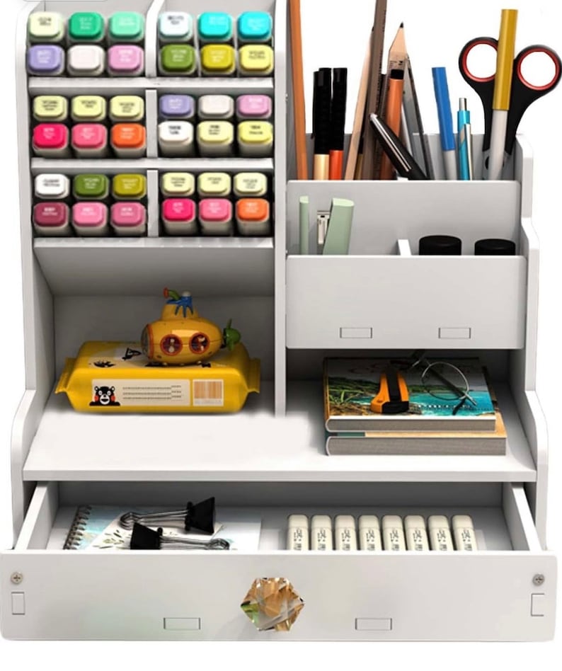 May include: White desktop organizer with multiple compartments for storing pens, pencils, markers, and other office supplies. It has a drawer for storing smaller items and a top shelf for displaying items.