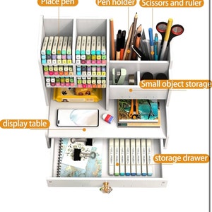 May include: White desktop organizer with a drawer, pen holder, and compartments for storing pens, markers, and other small items. The organizer has a small display table on top and a drawer for storing larger items.