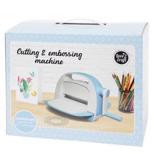 Puede incluir: Un juego de inicio de m&aacute;quina de corte y relieve en azul claro y blanco. La caja dice "Cutting & embossing machine" y "Love 2 Craft". El juego incluye una m&aacute;quina, troqueles y una tarjeta de muestra con un dise&ntilde;o floral.