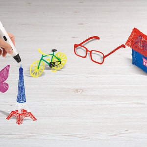 Pu&ograve; includere: Una penna 3D bianca crea modelli in plastica colorati, tra cui una farfalla, la Torre Eiffel, una bicicletta, occhiali e una casa. La Torre Eiffel &egrave; rossa, bianca e blu. La bicicletta &egrave; verde e gialla.