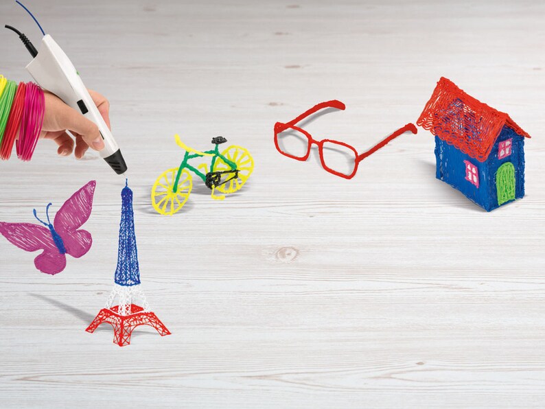 Pu&ograve; includere: Una penna 3D bianca crea modelli in plastica colorati, tra cui una farfalla, la Torre Eiffel, una bicicletta, occhiali e una casa. La Torre Eiffel &egrave; rossa, bianca e blu. La bicicletta &egrave; verde e gialla.