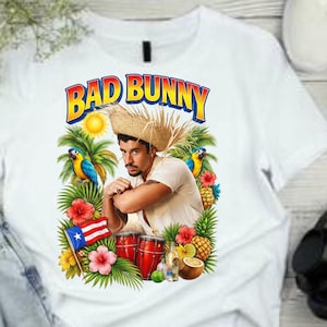Könnte beinhalten: Weißes T-Shirt mit einem farbenfrohen Grafikdesign, das einen Mann mit Strohhut vor tropischem Hintergrund zeigt, einschließlich Papageien, Blumen und einer puerto-ricanischen Flagge. Der Text "BAD BUNNY" ist darüber abgebildet.