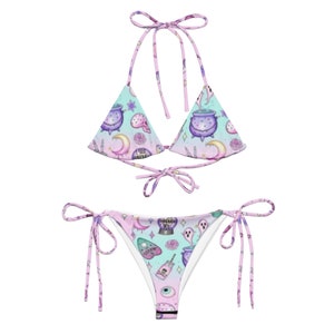 May include: A pink and blue bikini with a tie-side bottom. The bikini has a pattern of cauldrons, moons, eyes, and other witchy symbols.