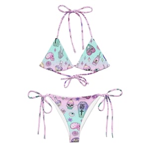 May include: A pink and blue bikini with a tie-side bottom. The bikini has a print of skulls, cupcakes, eyes, and other spooky and cute designs. The top is a triangle style with adjustable straps.