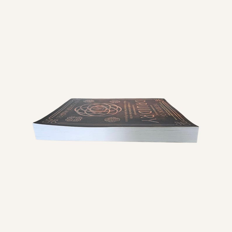 Op de afbeelding: Een hardcover boek getiteld "Druidry: The Book of the Ancient Wisdom" met een donkere kaft en koperkleurige reli&euml;fontwerpen. De pagina's van het boek zijn wit.