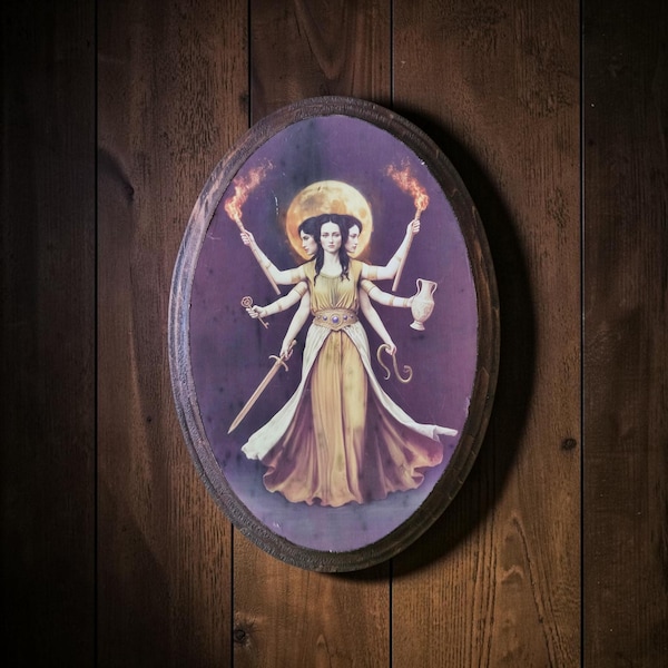 May include: An oval wall plaque featuring a print of a three-headed figure with six arms against a full moon background. The figure wears a yellow dress and holds a key, a sword, a pitcher, a snake, and two flaming torches in a purple setting.