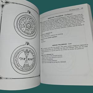 K&ouml;nnte beinhalten: Offenes Buch mit zwei detaillierten Illustrationen von Talismanen, die komplizierte geometrische Designs und Text aufweisen. Die Seite enth&auml;lt auch Text, der die Talismane beschreibt. Das Buch liegt auf einer gr&uuml;nen Oberfl&auml;che.