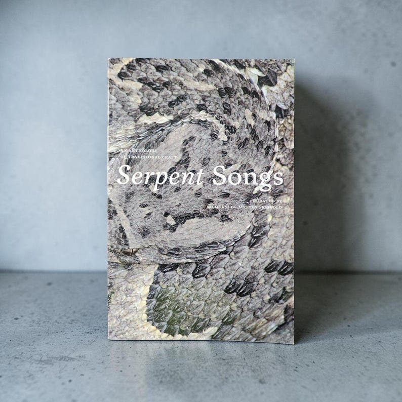 May include: A rectangular book titled Serpent Songs, an anthology of traditional craft curated by Nicholas de Matos Frisvold. The cover features a detailed, high-resolution photograph of grey, black, and white snake scales in a coiled pattern.
