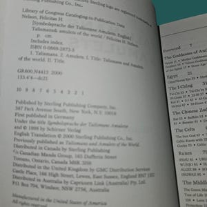 K&ouml;nnte beinhalten: Aufgeschlagenes Buch mit Text &uuml;ber Talismane und Amulette, einschlie&szlig;lich ISBN- und Library of Congress-Daten. Die Seiten sind wei&szlig; mit schwarzem Text, und der Titel ist sichtbar.