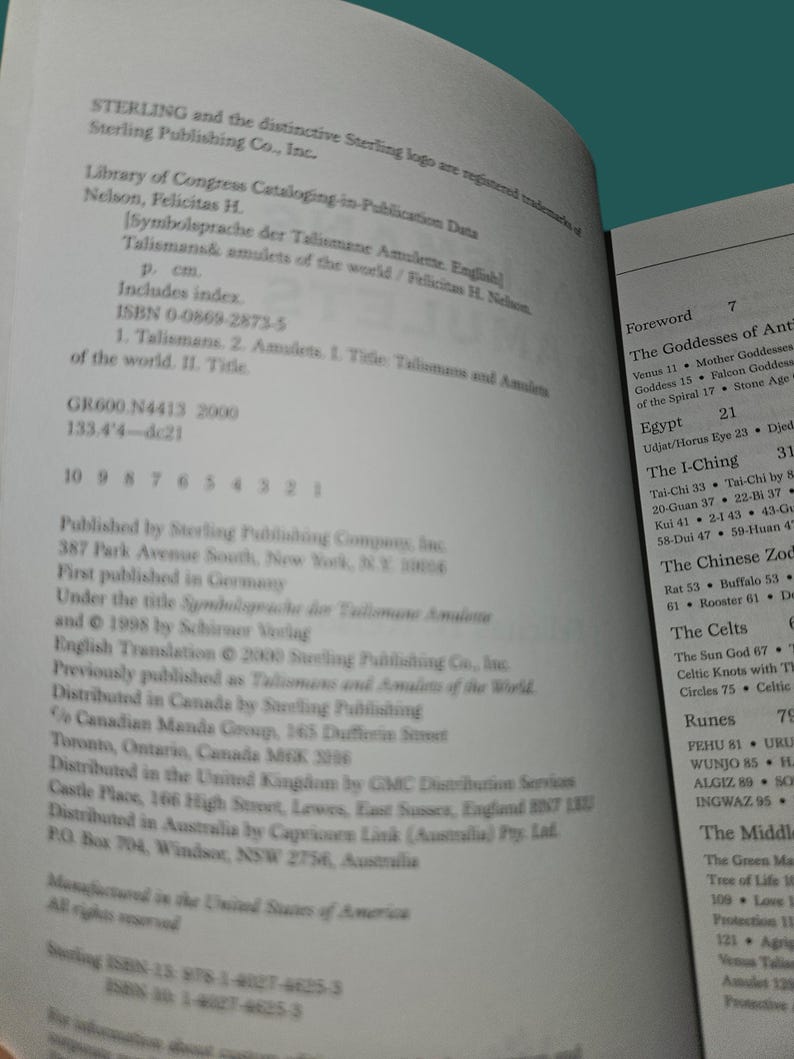 K&ouml;nnte beinhalten: Aufgeschlagenes Buch mit Text &uuml;ber Talismane und Amulette, einschlie&szlig;lich ISBN- und Library of Congress-Daten. Die Seiten sind wei&szlig; mit schwarzem Text, und der Titel ist sichtbar.