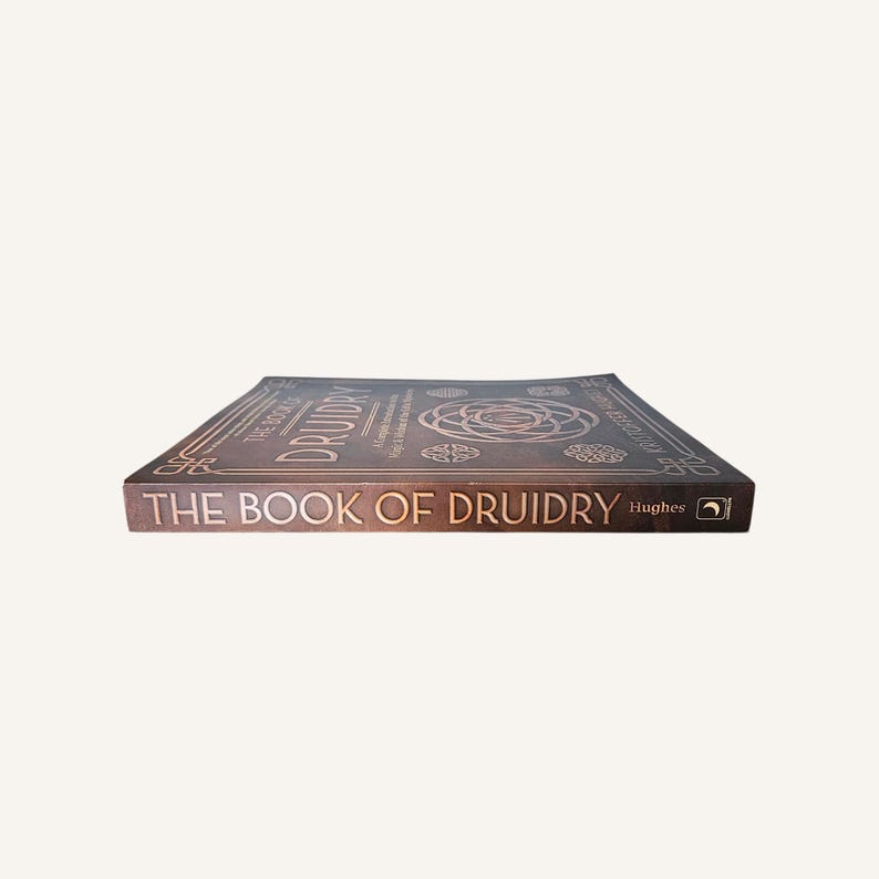 Op de afbeelding: Een bruin boek getiteld "THE BOOK OF DRUIDRY" met gouden letters. De cover heeft Keltische knoopontwerpen en de naam "Hughes". Het boek ligt plat en toont de cover en rug.