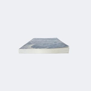 May include: A paperback book titled Serpent Songs with a blue and white cover featuring a textured, abstract design. The book is positioned horizontally, showing the white pages of the text block and the front cover edge against a plain background.