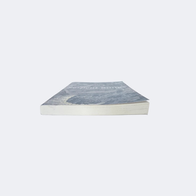 May include: A paperback book titled Serpent Songs with a blue and white cover featuring a textured, abstract design. The book is positioned horizontally, showing the white pages of the text block and the front cover edge against a plain background.