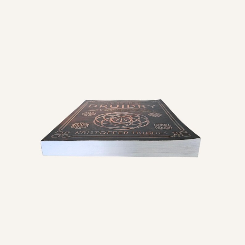Op de afbeelding: Een hardcover boek getiteld "The Book of Druidry" van Kristoffer Hughes. De omslag is donker met goudkleurige tekst en Keltische knoopontwerpen. Het boek ligt plat, met de pagina's zichtbaar.