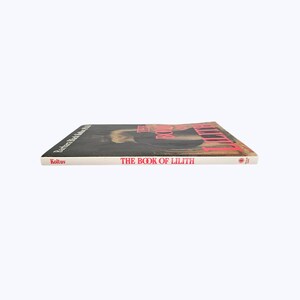 Pode incluir: Um livro de capa dura intitulado "THE BOOK OF LILITH" com letras vermelhas na lombada e na capa. O livro tem uma capa preta com uma ilustra&ccedil;&atilde;o e o nome da autora, Barbara Black Koltuv, impresso na lateral.