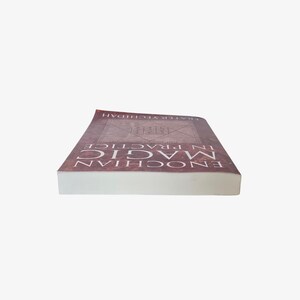 May include: A book titled "Enochian Magic in Practice" with a brown cover and white pages. The cover features a geometric design and the author's name. The book is lying on a white surface.
