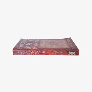 May include: A hardcover book titled "Enochian Magic in Practice" by Frater Yechidah. The book has a reddish-brown cover with the title in white and a geometric design. The book is lying flat.