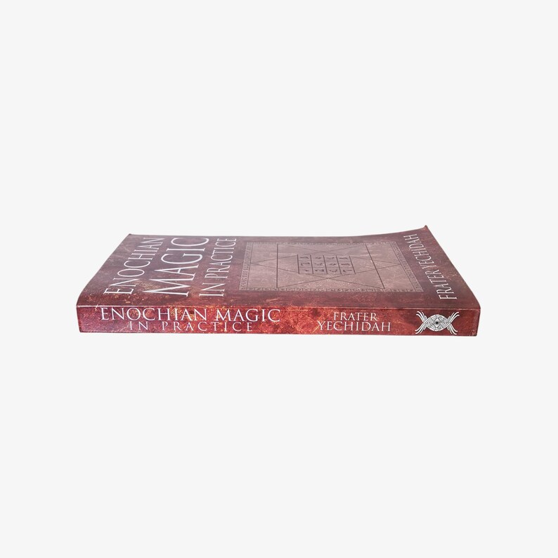 May include: A hardcover book titled "Enochian Magic in Practice" by Frater Yechidah. The book has a reddish-brown cover with the title in white and a geometric design. The book is lying flat.