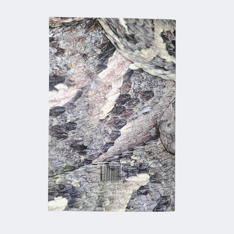 May include: A rectangular book cover featuring a high-resolution, close-up photograph of textured, overlapping snake scales in shades of gray, black, and tan. A barcode is printed near the bottom center, with small text visible below it.