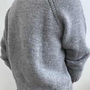 May include: A gray knitted sweater with a round neckline and long sleeves. The sweater has a ribbed hem and cuffs.