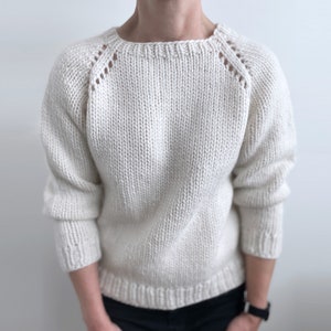 May include: A white knitted sweater with a round neckline and long sleeves. The sweater has a textured knit and a subtle pattern on the shoulders.
