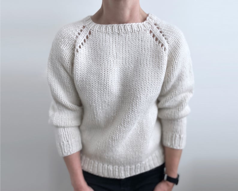 May include: A white knitted sweater with a round neckline and long sleeves. The sweater has a textured knit and a subtle pattern on the shoulders.