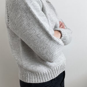 May include: A gray knitted sweater with long sleeves and a crew neck.