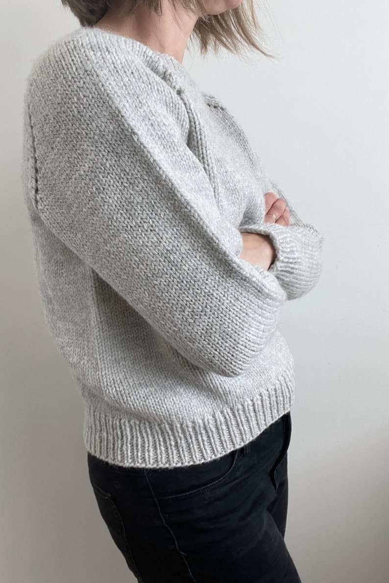 May include: A gray knitted sweater with long sleeves and a crew neck.