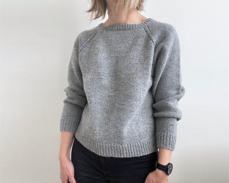 May include: A gray knitted sweater with a round neckline and raglan sleeves.