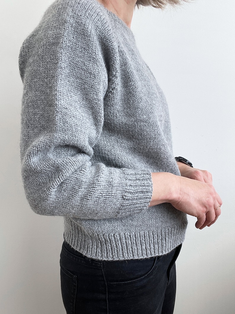 May include: A gray knitted sweater with long sleeves and a round neckline.