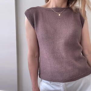 Może przedstawiać: Beżowy, bezrękawnikowy top z dzianiny z okrągłym dekoltem i delikatnym złotym łańcuszkiem.