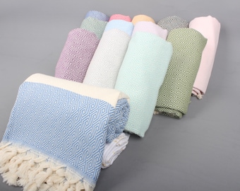 May include: A collection of rolled up Turkish towels in various colors, including light blue, pink, green, and white. The towels have a diamond pattern and fringe.