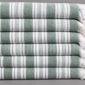 May include: A stack of six green and white striped towels with white fringe. The towels are folded and stacked on a gray surface.