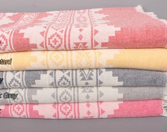 May include: A stack of five patterned Turkish towels in different colors: red, mustard yellow, navy blue, dark gray, and pink. The towels have a geometric design and fringe edges.