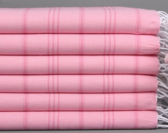 Può includere: Una pila di sei asciugamani turchi rosa con un motivo a righe. Ogni asciugamano ha una striscia rosa chiaro al centro e frange bianche alle estremità. Gli asciugamani sono ben piegati e impilati uno sopra l'altro.