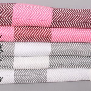 May include: A stack of four woven cotton throws with fringe edges. The top throw is pink and burgundy, the second is burgundy and pink, the third is dark grey and white, and the bottom is grey and dark grey.