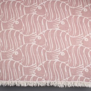 May include: A pink and white patterned throw blanket with a fringe border. The pattern features stylized fish.