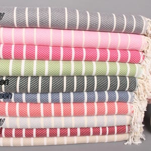 Peut inclure: Une pile de dix serviettes rayées de différentes couleurs, dont gris foncé, rose, fuchsia, vert, vert foncé, vert pétrole, corail, gris clair, rouge foncé et beige. Les serviettes sont pliées et empilées les unes sur les autres, avec les extrémités des serviettes qui dépassent sur les côtés. Les serviettes sont faites d'un matériau doux et absorbant et sont parfaites pour une utilisation à la plage, à la piscine ou au spa.