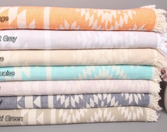 May include: A stack of seven patterned towels in various colors, including orange, light gray, beige, turquoise, lilac, navy, and khaki green. The towels are folded and stacked on top of each other, with the top towel being orange and the bottom towel being khaki green.