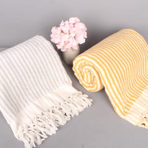 May include: Two striped towels with fringe. One towel is white with light blue stripes and the other is white with yellow stripes.
