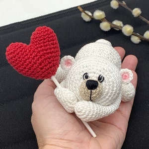 May include: A white crocheted polar bear holding a red crocheted heart on a stick.
