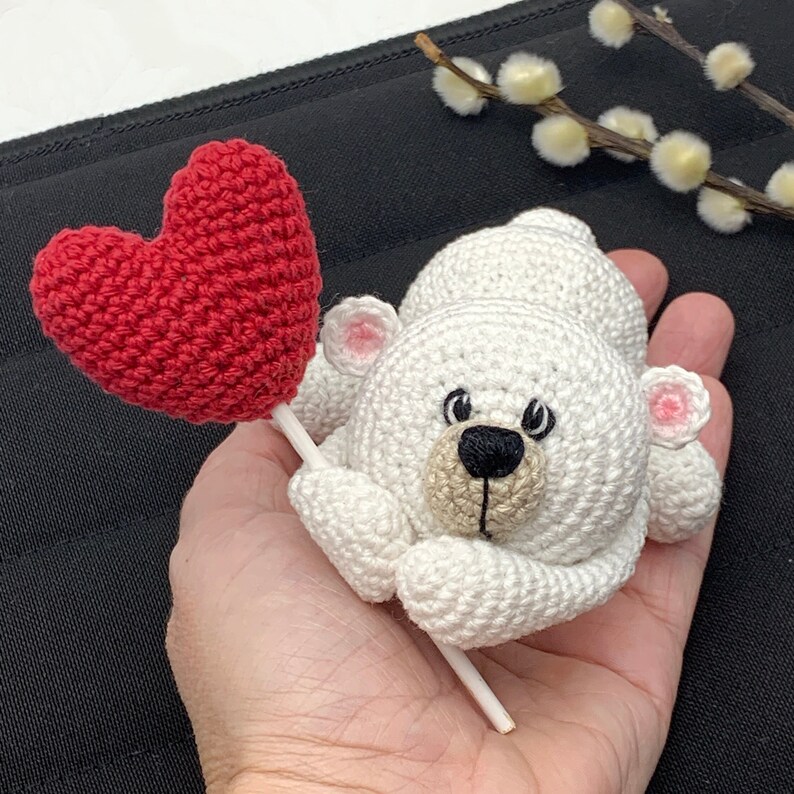 May include: A white crocheted polar bear holding a red crocheted heart on a stick.