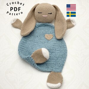 May include: Crocheted bunny lovey with a blue blanket and beige ears and feet. The bunny has a heart on its chest. The lovey is a handmade crochet pattern.