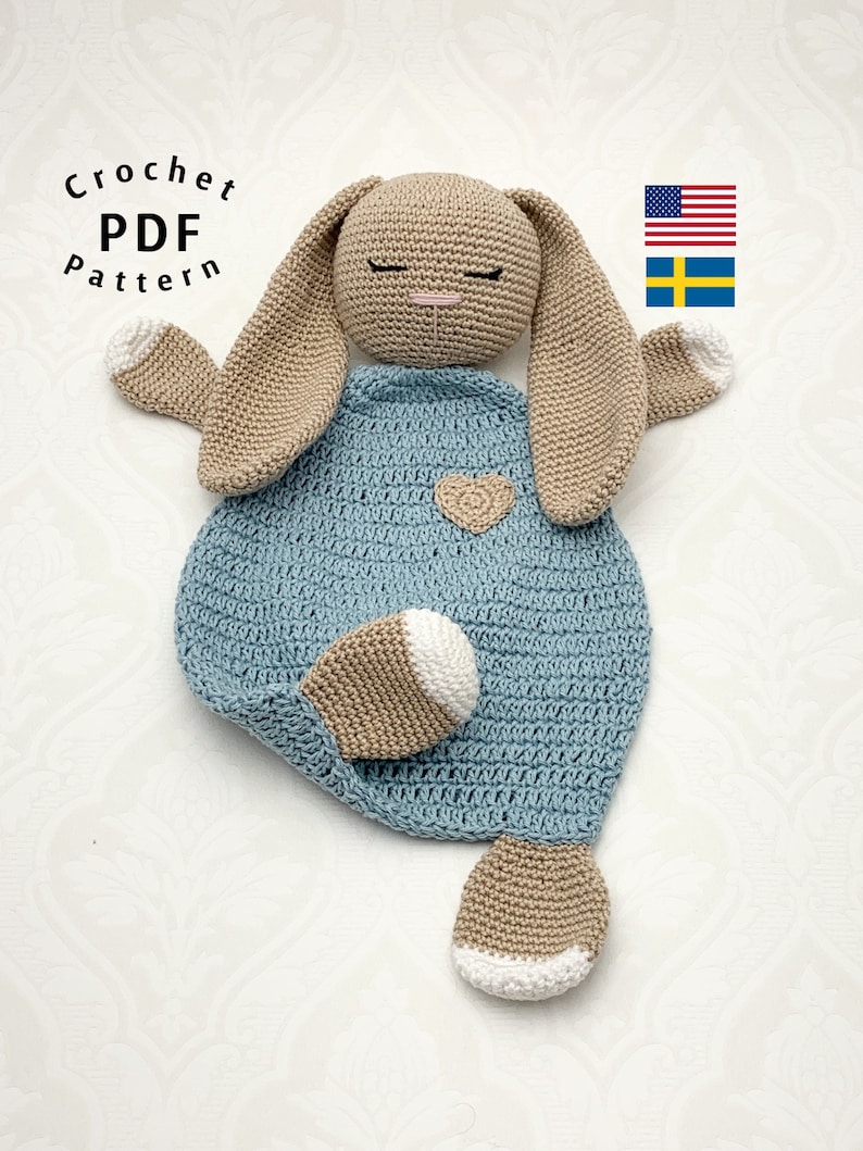 May include: Crocheted bunny lovey with a blue blanket and beige ears and feet. The bunny has a heart on its chest. The lovey is a handmade crochet pattern.