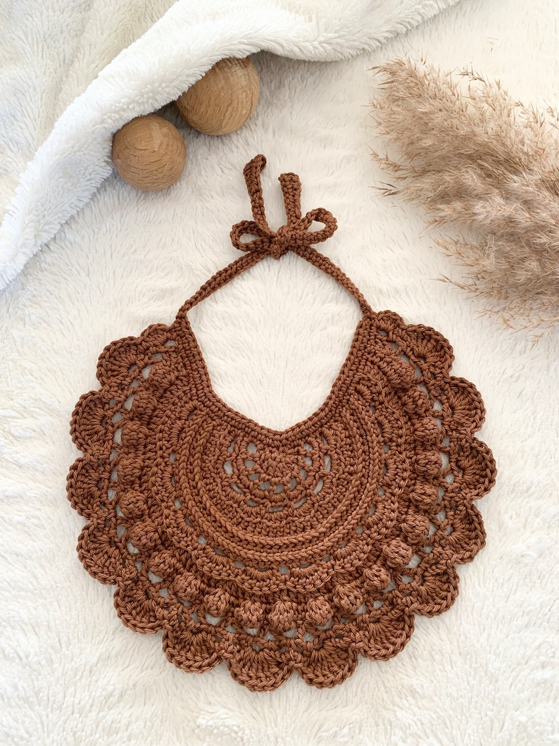 May include: A brown crocheted bib with a scalloped edge and a bow at the top.